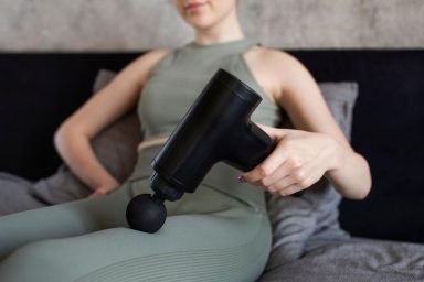 A person who is sore using a TOLOCO massage gun, a percussion-based device that stands out among recovery tools for deep muscle relief.