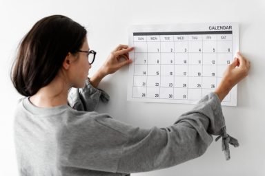 A woman placing a 2026 desk calendar on a wall to track her daily workout habits.
